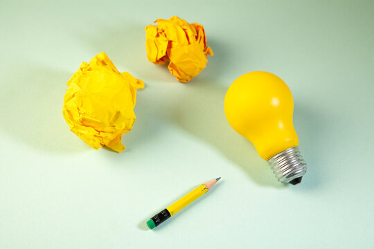 Yellow crumpled paper light bulb and pencil on a green background