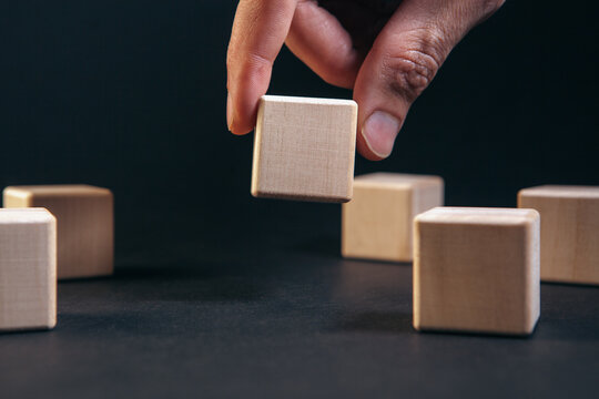 Closeup of human hand playing wooden blocks game on black background.