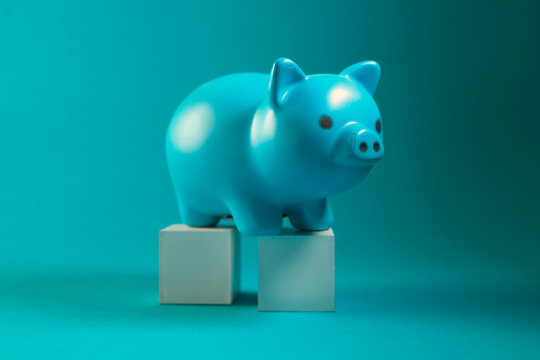 Blue piggy bank on a white cube on a turquoise background