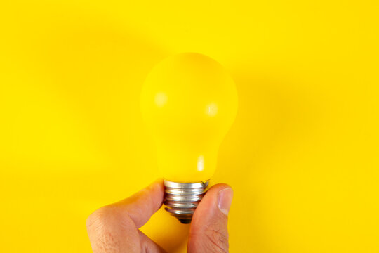 Hand holding a yellow light bulb on a yellow background with copy space
