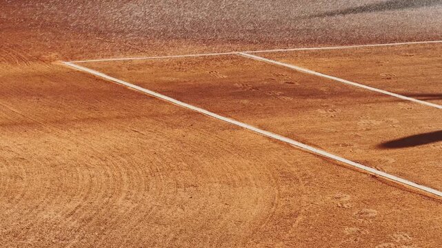 Clay tennis court being watered before play, with wet orange surface, white boundary lines, and maintenance preparation for a sports match.
