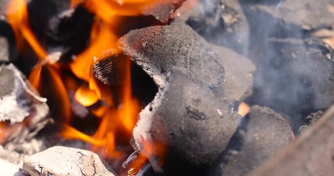 charcoal and twigs   burning in a barbecue campfire in the park, details of twigs and charcoal with orange flames and smoke from insufficient air for combustion, outdoor activity