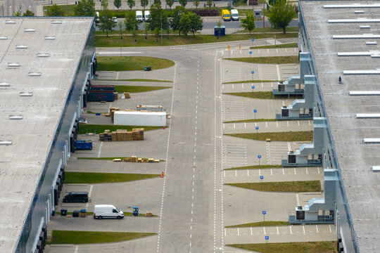 Aerial view of a modern logistics center with loading docks, industrial warehouses, and a white van parked on the asphalt road in Warsaw, Masovian Voivodeship, Poland.