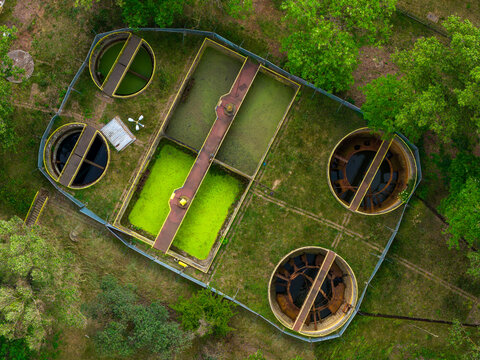 Aerial view of a water treatment facility featuring circular sedimentation tanks and rectangular basins surrounded by lush green trees in Warsaw, Masovian Voivodeship, Poland.