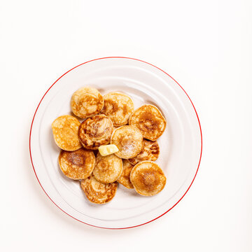 Dutch poffertjes, small pancakes, arranged on a white plate with a red rim, featuring a pat of butter on top for added flavor. Top view