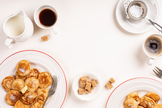 Dutch poffertjes, small pancakes, arranged on plates with coffee, cream, and sugar cubes on a light-colored table setting. Top view with copy space.