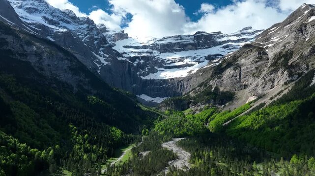 Cirque de Gavarnie towering snowy walls and waterfall above green forested valley and river