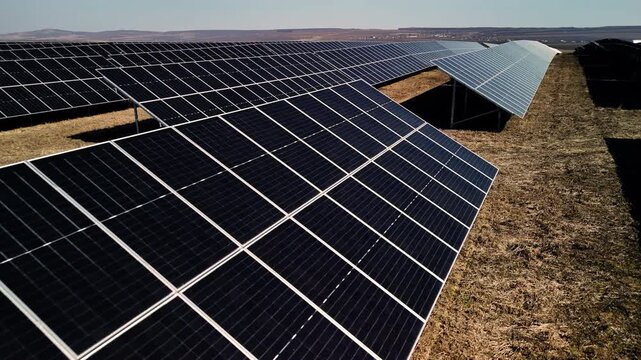 Solar panels arranged in rows on a grassy field under a clear blue sky, showcasing renewable energy technology in a vast outdoor setting