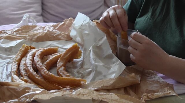 Person dipping a delicious churro into a hot chocolate glass for a typical spanish breakfast, food and cuisine concept
