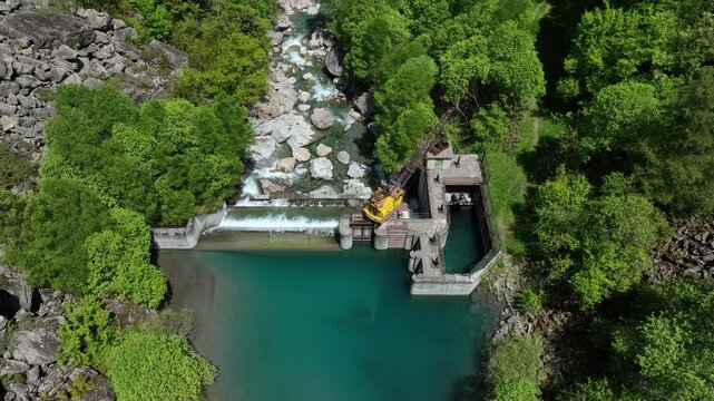 Aerial view of small hydroelectric dam and weir on turquoise mountain river in green Pyrenees forest