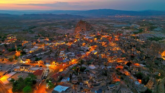 Aerial view of Uchisar at night, Cappadocia, Turkey. Warm lights trace village streets around cave houses and rocky hills.