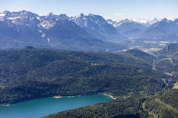 Fototapeta premium Scenic view of Lake Kochel, forests and snowcapped Alps from Herzogstand mountain on a sunny spring day