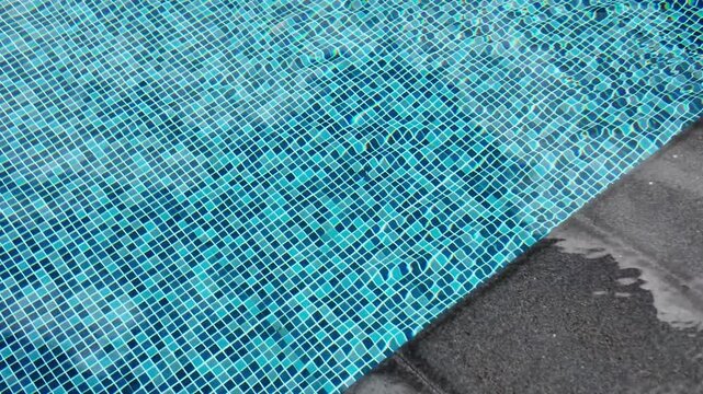 Top view of swimming pool with blue mosaic tiles and water ripples