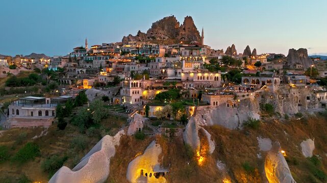 Drone view of Uchisar at night, Cappadocia, Turkey. Illuminated streets, cave homes and Uchisar Castle give a dramatic evening view.