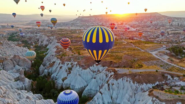 Drone view of Rose Valley, Cappadocia, Turkey. A colourful hot air balloon rises over fairy chimneys and layered rock formations in the early morning light.