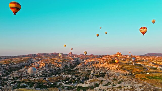 Aerial view of Rose Valley, Cappadocia, Turkey. Hot air balloons float over the canyon landscape and sunlit rock formations.