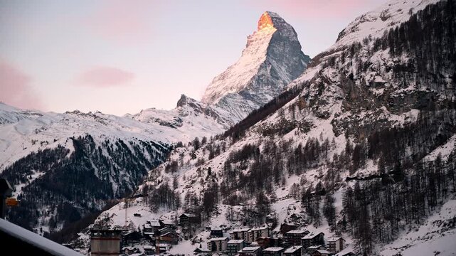 Timelapse view of the Matterhorn above Zermatt, Switzerland, during early morning twilight. Snow covered ski resort landscape with alpine village, winter tourism and holiday atmosphere.