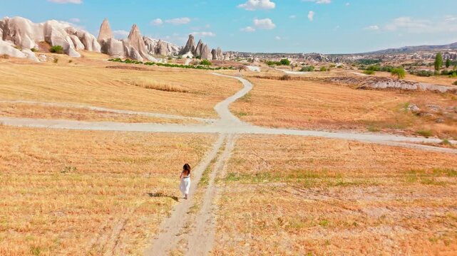 . Female visitor running on a scenic path in Cappadocia, Turkey countryside. Golden fields and distant fairy chimneys line a peaceful rural trail.