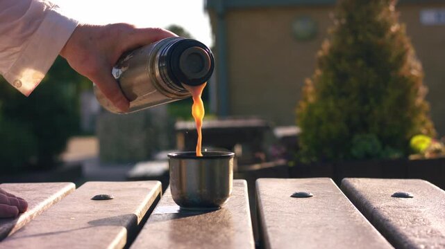 Pouring hot drink from flask on outside wooden table