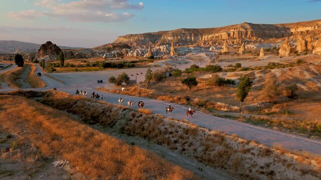 Aerial view of Rose Valley, Cappadocia, Turkey at sunset. Tourists quad biking across dusty trails below golden cliffs and fairy chimneys.