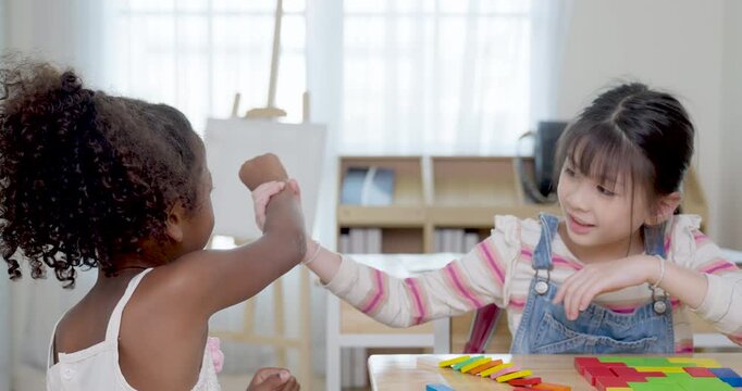 Two elementary girls sort colorful blocks at wooden desk, playful back to school activity builds peer support, logic practice, friendship, confidence, participation, early math readiness skill