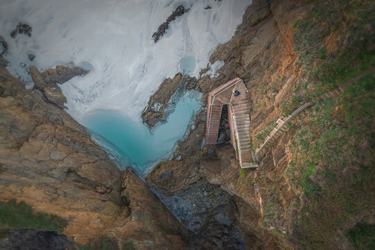 Aerial view of the stone staircase carved into rugged cliffs leading down to a turquoise cove and white sand beach at Ermita de Santa Comba, Covas, La Coruna, Spain.