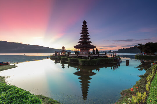 Colorful sunrise with dramatic sun rays and perfect water reflections at the historic Ulun Danu Beratan Temple in Bali, Indonesia
