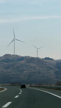 Car driving on a scenic highway with wind turbines in the landscape at background