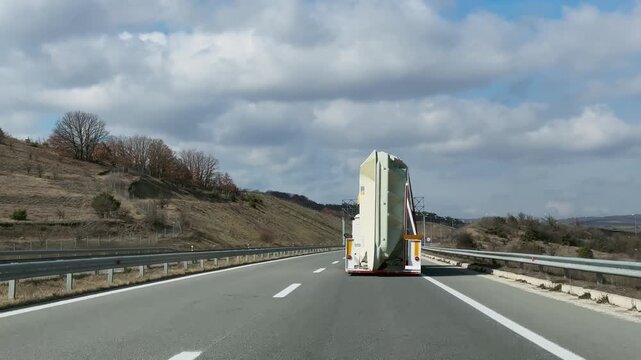 Large truck carrying oversized swimming pool equipment drives along a winding highway through a rural landscape