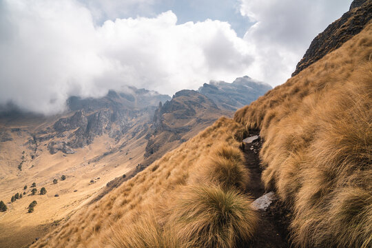 Scenic hiking trail through grassy slopes of Popocat&eacute;petl Mexico with dramatic clouds and rugged mountain landscape