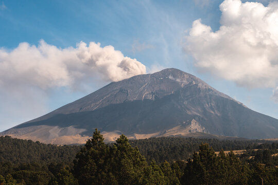 Majestic view of Popocat&eacute;petl volcano in Mexico with smoke plume rising above forested landscape during daytime adventure