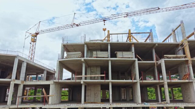Unfinished concrete building under construction multi level skeletal floors with exposed columns and beams, tower crane hoisting materials, crew installing