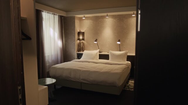 Empty modern hotel room with large double bed being revealed from behind dark wooden door. Perfect for hospitality marketing, travel agency promotions, or real estate showcases, wide tracking shot