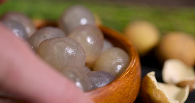 The whitish flesh of a longan in a cup, this tropical longan without a shell is presented in the form of a pile of fruits in a wooden container on a dark background.