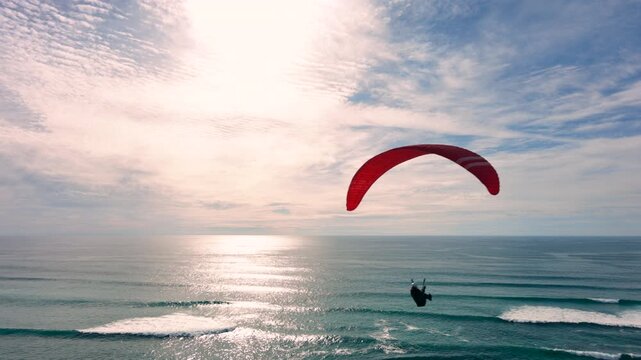 Drone shot of a man paragliding above the ocean, water
