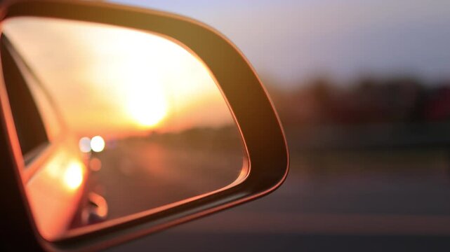 The sun is reflected in the mirror, evening road. View in the side rear view mirror of a red car driving along the highway