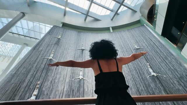 Woman posing spreading hands at Dubai mall waterfall with flying sculptures