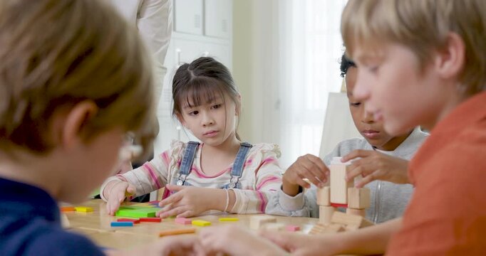 Multicultural elementary children use wooden blocks and color tiles at desk, building teamwork, STEM activity, peer friendship, study habit, back to school participation in bright primary classroom