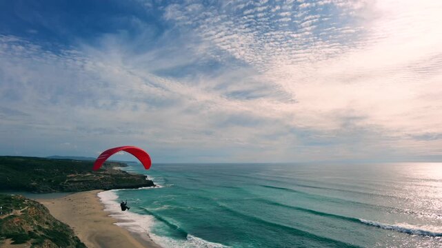 Drone shot of a man paragliding above the ocean, water