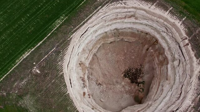 Top down drone footage inside a large dry sinkhole, showing steep eroded walls, cracked soil layers, geological textures, natural ground collapse, and karst terrain from above.