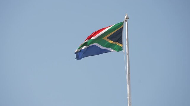 The South African flag flutters gently on a flagpole against a clear blue sky. Ideal for patriotic or cultural content.