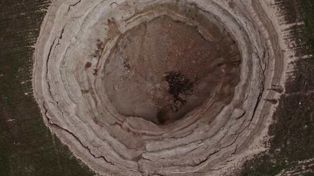 Top down drone footage inside a large dry sinkhole, showing steep eroded walls, cracked soil layers, geological textures, natural ground collapse, and karst terrain from above.