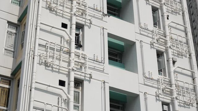 Outer facade view of a modern apartment building with white walls and external piping network.