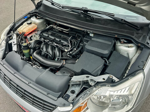 Car engine viewed from the top with various components visible in a gray vehicle with a clean and organized appearance on a concrete surface