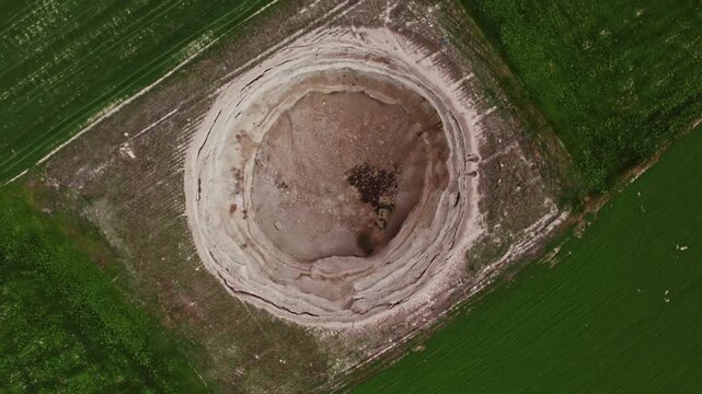 Top down drone footage inside a large dry sinkhole, showing steep eroded walls, cracked soil layers, geological textures, natural ground collapse, and karst terrain from above.