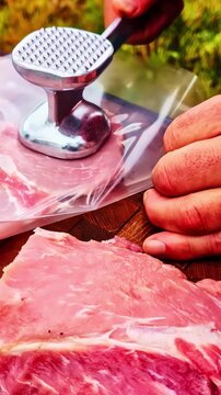 Male hands pounding fresh pork loin slices with a metal hammer on a wooden cutting board outdoors
