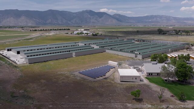 Orbiting drone perspective of a large, modern self-storage facility complex powered by solar panels, set against a vast rural landscape with majestic mountains in the distant background