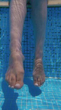 Underwater shot of feet immersed in a blue swimming pool, capturing the serene feel of summer relaxation, vertical video