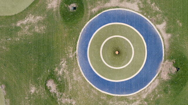 Aerial view of the circular target at Chi Chi - The Golf Venue with concentric blue and green rings on a grassy field scattered with golf balls in Utrecht, Utrecht, Netherlands.