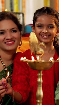 Closeup of Happy Indian Family of Four in Traditional Attire Lighting Diya or Samai Together on Hindu Festival Day at home